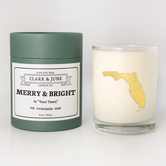 Double wicked soy candle in a 13.5 oz tumbler with the state of Floridaprinted in 22k gold foil on the face. Green cylinder packaging with Merry & Bright in "Your Town"on the label. SEO Text – Drinking glass, soy wax candle, Christmas Candle, hand poured, small batch, scented candle, Woman Owned, local candle, Housewarming present, gives back, charity, community candle, becomes a cocktail glass, closing gift. 