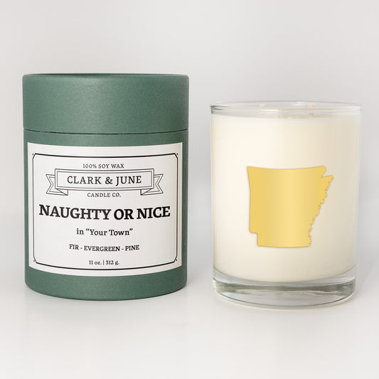 Double wicked soy candle in a 13.5 oz tumbler with the state of Arkansasprinted in 22k gold foil on the face. Green cylinder packaging with Naughty or Nice in "Your Town" on the label. SEO Text – Drinking glass, soy wax candle, Christmas Candle, hand poured, small batch, scented candle, Woman Owned, local candle, Housewarming present, gives back, charity, community candle, becomes a cocktail glass, closing gift. 
