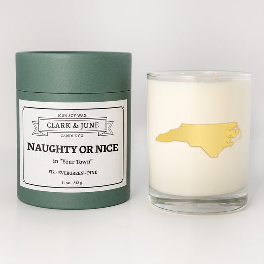 Double wicked soy candle in a 13.5 oz tumbler with the state of North Carolinaprinted in 22k gold foil on the face. Green cylinder packaging with Naughty or Nice in "Your Town" on the label. SEO Text – Drinking glass, soy wax candle, Christmas Candle, hand poured, small batch, scented candle, Woman Owned, local candle, Housewarming present, gives back, charity, community candle, becomes a cocktail glass, closing gift. 