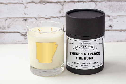 Double wicked soy candle in a 13.5 oz tumbler with the state of Arkansas printed in 22k gold foil on the face. Black cylinder packaging with “There’s No Place Like Home” on the label. SEO Text – Drinking glass, soy wax candle, Arkansas candle, hand poured, small batch, scented candle, Woman Owned, local candle, Housewarming present, gives back, charity, community candle, becomes a cocktail glass, closing gift. 