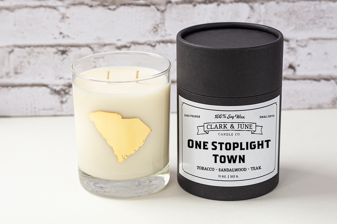 Double wicked soy candle in a 13.5 oz tumbler with the state of South Carolina printed in 22k gold foil on the face. Black cylinder packaging with “One Stoplight Town” on the label. SEO Text – Drinking glass, soy wax candle, Alabama candle, hand poured, small batch, scented candle, Woman Owned, local candle, Housewarming present, gives back, charity, community candle, becomes a cocktail glass, closing gift. 