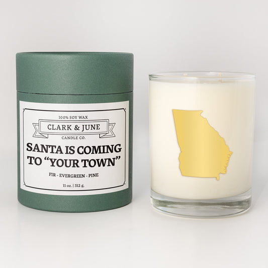 Double wicked soy candle in a 13.5 oz tumbler with the state of Georgiaprinted in 22k gold foil on the face. Green cylinder packaging with Santa is Coming to "Your Town"on the label. SEO Text – Drinking glass, soy wax candle, Christmas Candle, hand poured, small batch, scented candle, Woman Owned, local candle, Housewarming present, gives back, charity, community candle, becomes a cocktail glass, closing gift. 