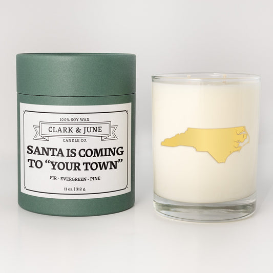 Double wicked soy candle in a 13.5 oz tumbler with the state of North Carolinaprinted in 22k gold foil on the face. Green cylinder packaging with Santa is Coming to "Your Town"on the label. SEO Text – Drinking glass, soy wax candle, Christmas Candle, hand poured, small batch, scented candle, Woman Owned, local candle, Housewarming present, gives back, charity, community candle, becomes a cocktail glass, closing gift. 