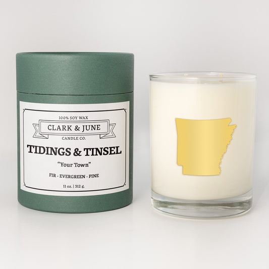 Double wicked soy candle in a 13.5 oz tumbler with the state of Arkansasprinted in 22k gold foil on the face. Green cylinder packaging with Tidings & Tinsel on the label. SEO Text – Drinking glass, soy wax candle, Christmas Candle, hand poured, small batch, scented candle, Woman Owned, local candle, Housewarming present, gives back, charity, community candle, becomes a cocktail glass, closing gift. 