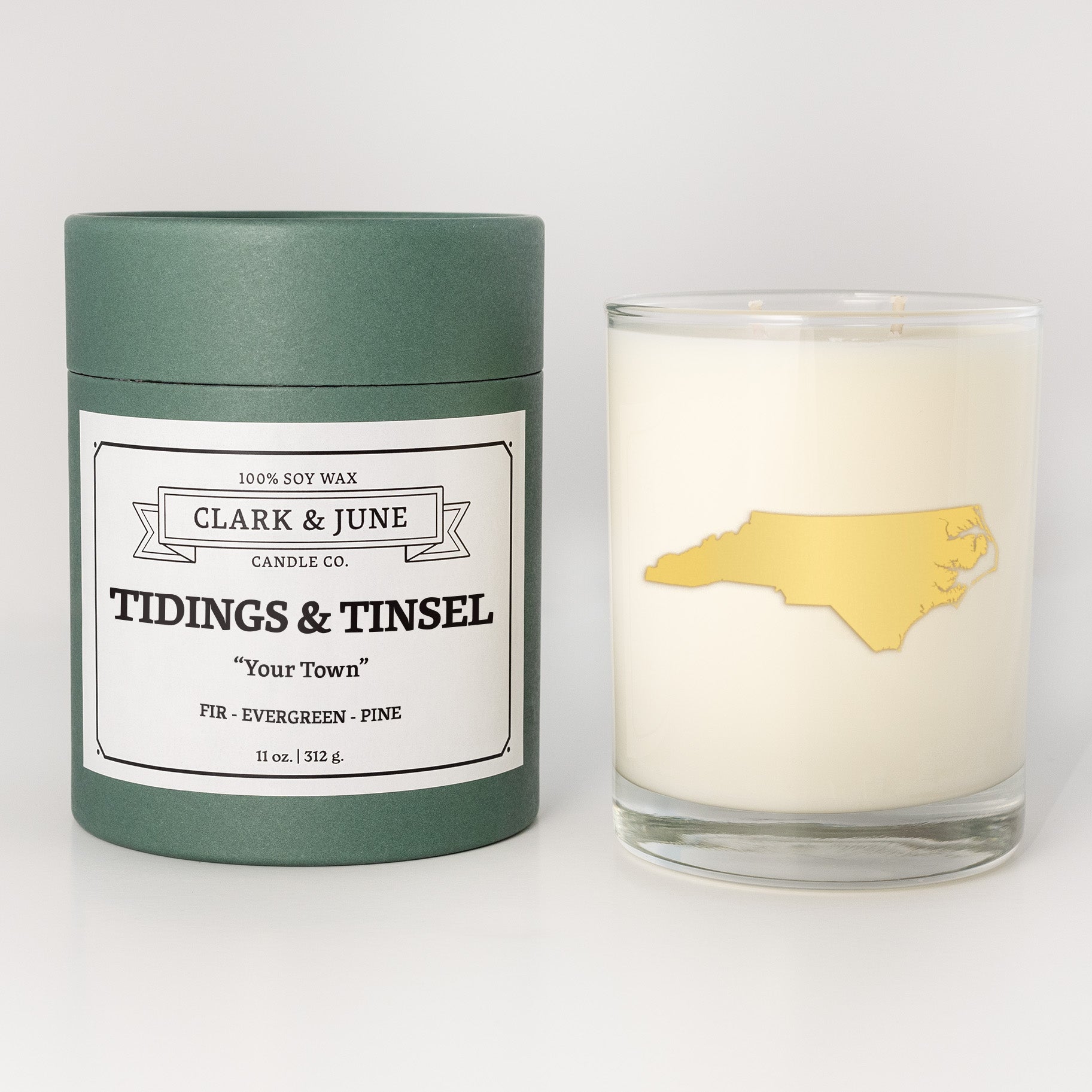 Double wicked soy candle in a 13.5 oz tumbler with the state of   North Carolina printed in 22k gold foil on the face. Green cylinder packaging with Tidings & Tinsel in "Your Town" on the label. SEO Text â€“ Drinking glass, soy wax candle, Christmas Candle, hand poured, small batch, scented candle, Woman Owned, local candle, Housewarming present, gives back, charity, community candle, becomes a cocktail glass, closing gift. 
