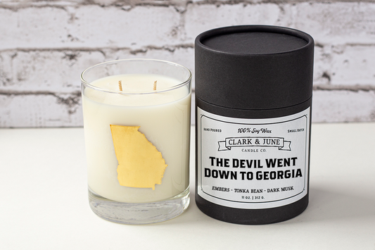 Double wicked soy candle in a 13.5 oz tumbler with the state of Georgia printed in 22k gold foil on the face. Black cylinder packaging with “The Devil Went Down to Georgia” on the label. SEO Text – Drinking glass, soy wax candle, Alabama candle, hand poured, small batch, scented candle, Woman Owned, local candle, Housewarming present, gives back, charity, community candle, becomes a cocktail glass, closing gift. 