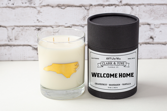 Double wicked soy candle in a 13.5 oz tumbler with the state of North Carolina printed in 22k gold foil on the face. Black cylinder packaging with “Welcome Home” on the label. SEO Text – Drinking glass, soy wax candle, North Carolina candle, hand poured, small batch, scented candle, Woman Owned, local candle, Housewarming present, gives back, charity, community candle, becomes a cocktail glass, closing gift.