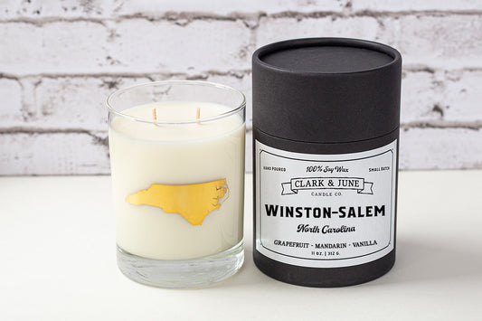 Double wicked soy candle in a 13.5 oz tumbler with the state of North Carolina printed in 22k gold foil on the face. Black cylinder packaging with “Winston-Salem” on the label. SEO Text – Drinking glass, soy wax candle, North Carolina candle, hand poured, small batch, scented candle, Woman Owned, local candle, Housewarming present, gives back, charity, community candle, becomes a cocktail glass, closing gift.
