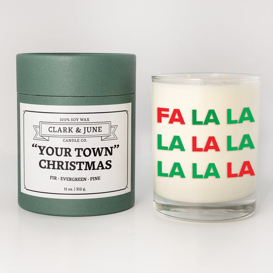 Double wicked soy candle in a 13.5 oz tumbler with Fa La La printed on the face. Green cylinder packaging with "Your Town" Christmas"on the label. SEO Text – Drinking glass, soy wax candle, Christmas Candle, hand poured, small batch, scented candle, Woman Owned, local candle, Housewarming present, gives back, charity, community candle, becomes a cocktail glass, closing gift. 