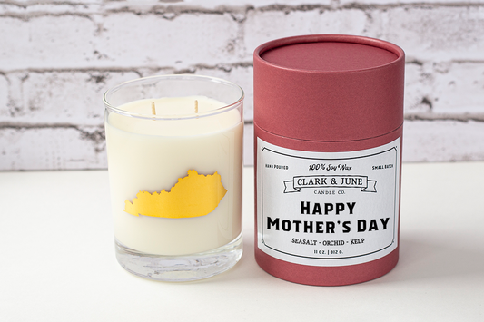 Double wicked soy candle in a 13.5 oz tumbler with the state of Kentucky printed in 22k gold foil on the face. Black cylinder packaging with “Happy Mother’s Day” on the label. SEO Text – Drinking glass, soy wax candle, Kentucky candle, hand poured, small batch, scented candle, Woman Owned, local candle, Housewarming present, gives back, charity, community candle, becomes a cocktail glass, closing gift. 